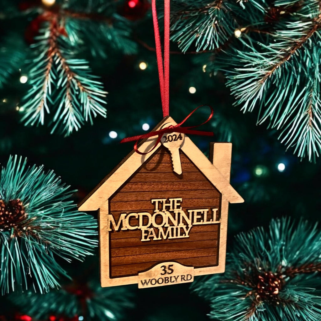 Wooden house-shaped ornament with 'The McDonnell Family' text hanging on a Christmas tree.
