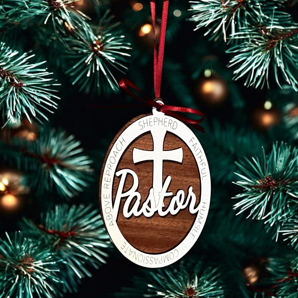 Ornament with 'Pastor' and cross design hanging on a Christmas tree.