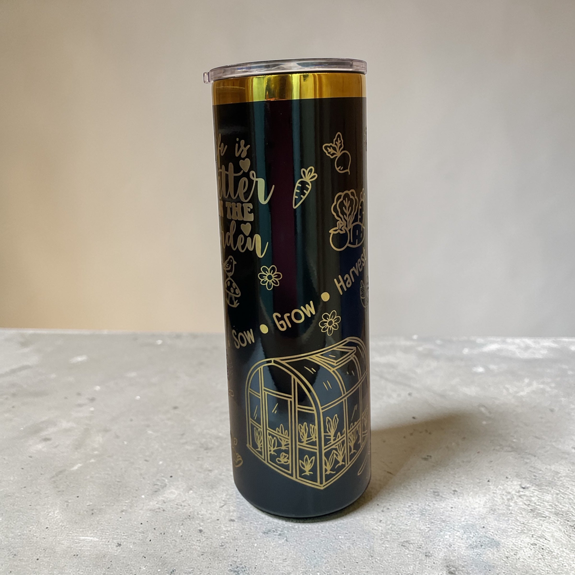 Black tumbler with gold designs and text on a light gray surface