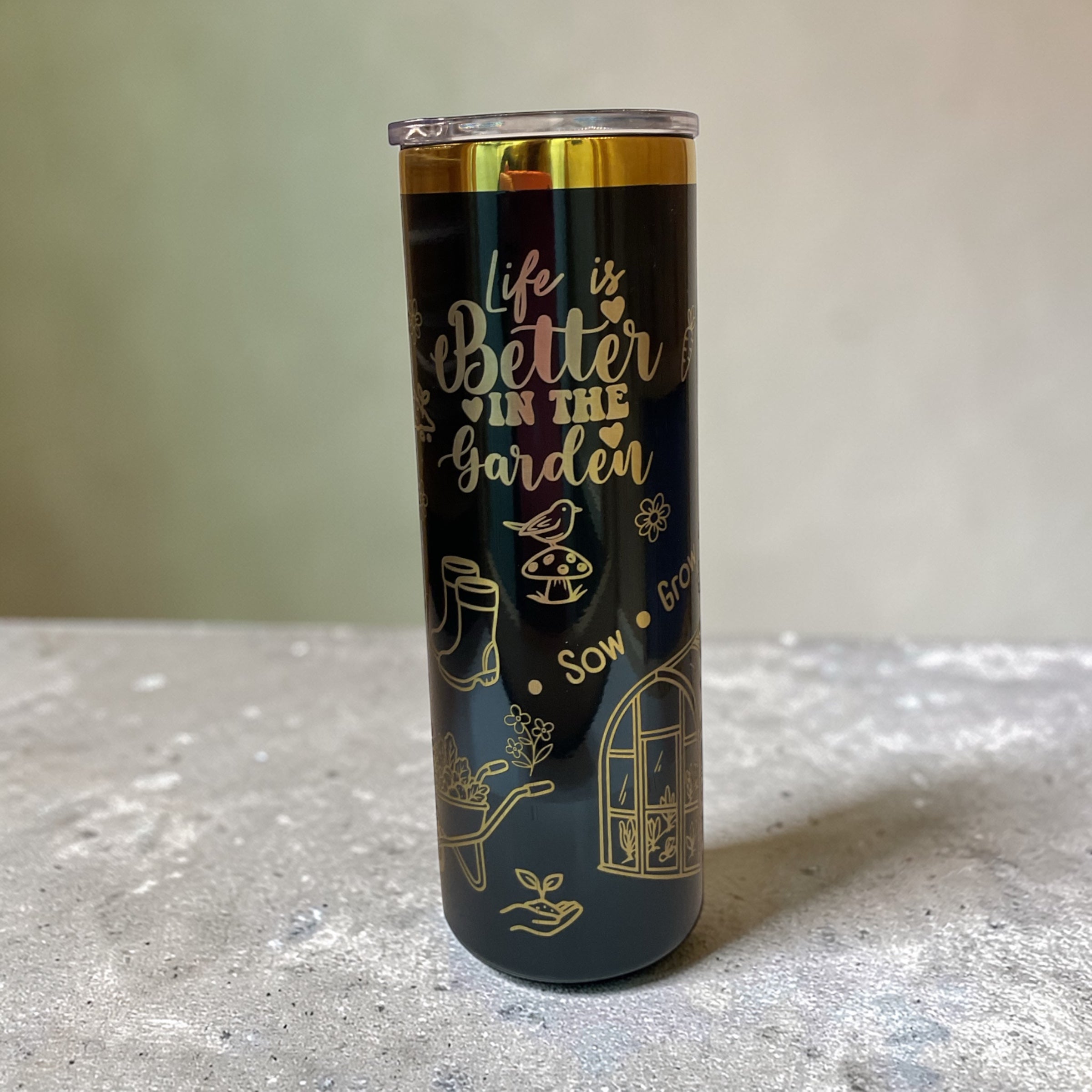 Tumbler with 'Life is Better in the Garden' text and gardening-themed illustrations on a neutral background.