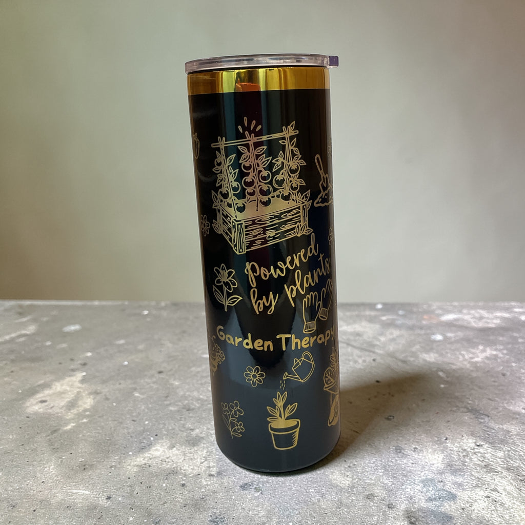 Tumbler with gold garden-themed design and text on a gray surface