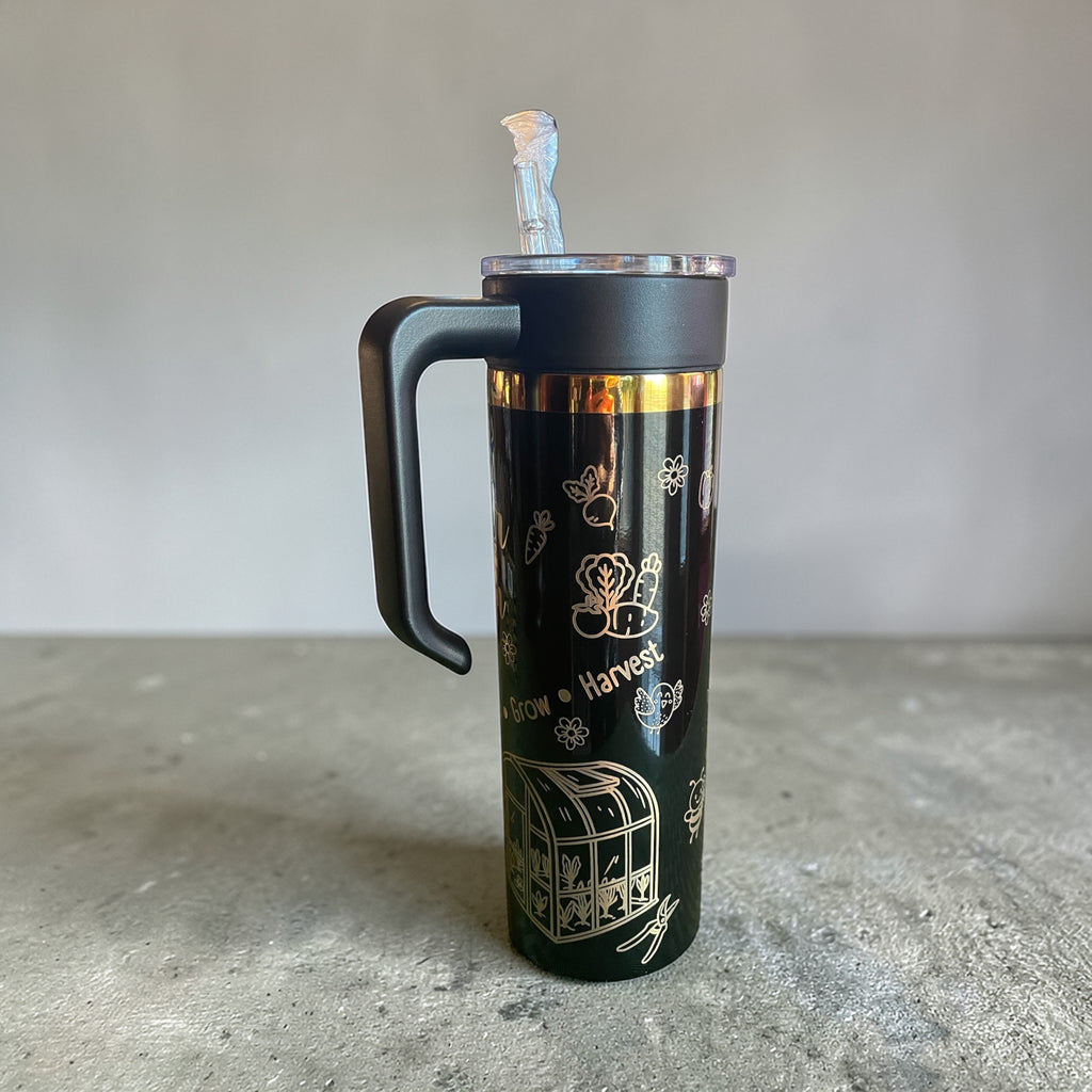 Black insulated tumbler with gold designs on a gray surface