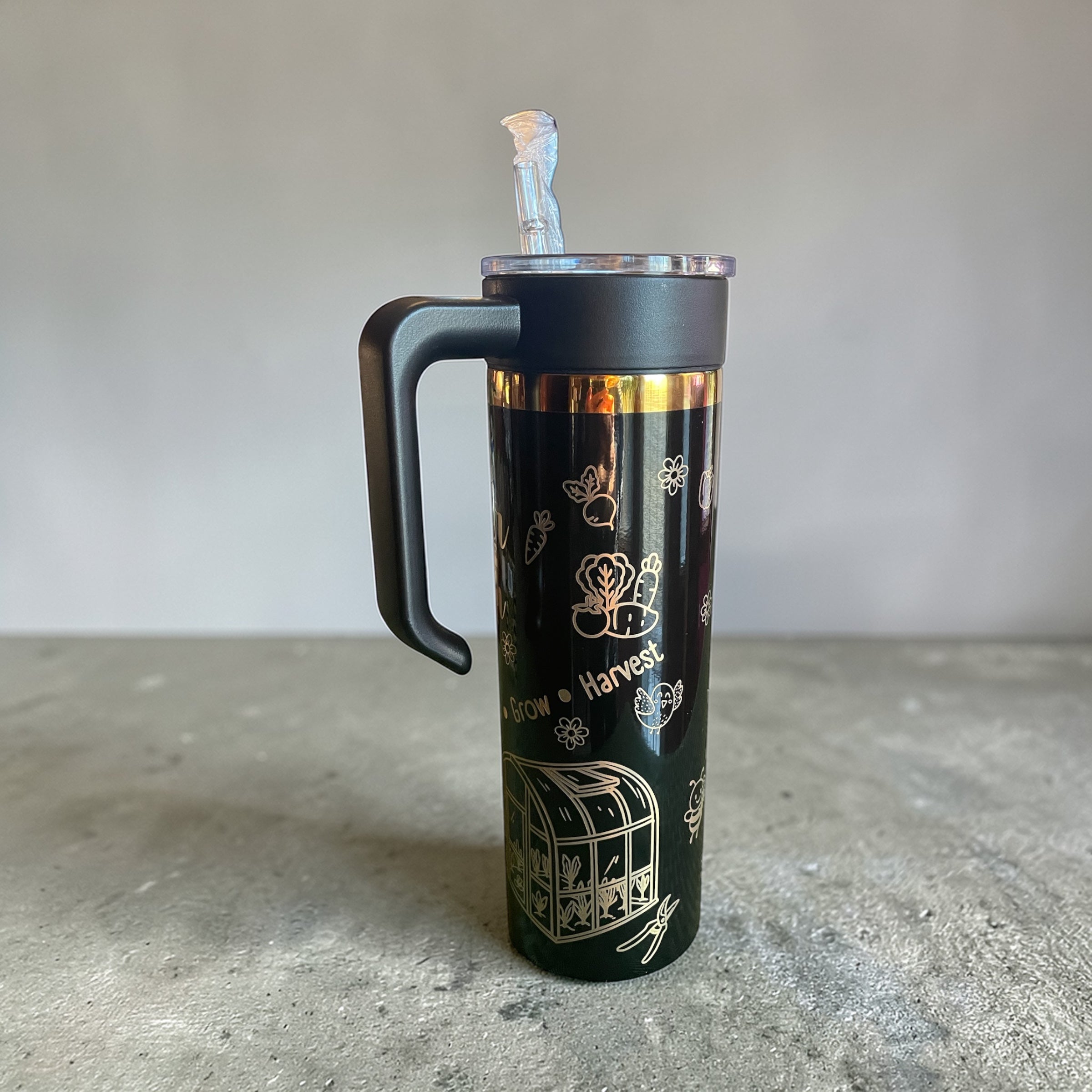 Black insulated tumbler with gold designs on a gray surface