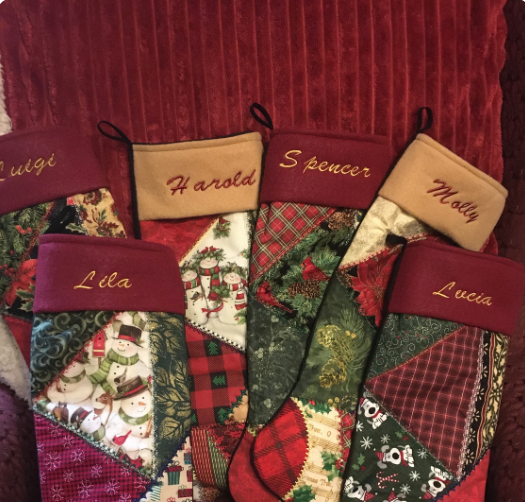 Set of personalized Christmas stockings with names embroidered on them against a red textured background.