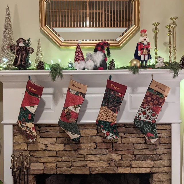 Four Christmas stockings hanging on a stone fireplace with decorative items above.