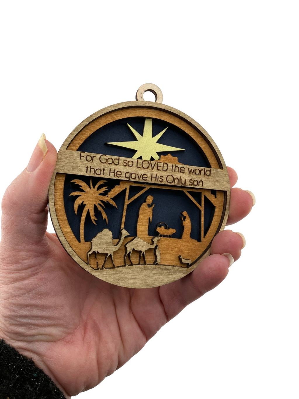 Close-up of handcrafted Christian Christmas ornament with nativity scene and scripture engraving.