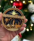Laser-cut wooden nativity ornament engraved with John 3:16 Bible verse, hanging on a Christmas tree.