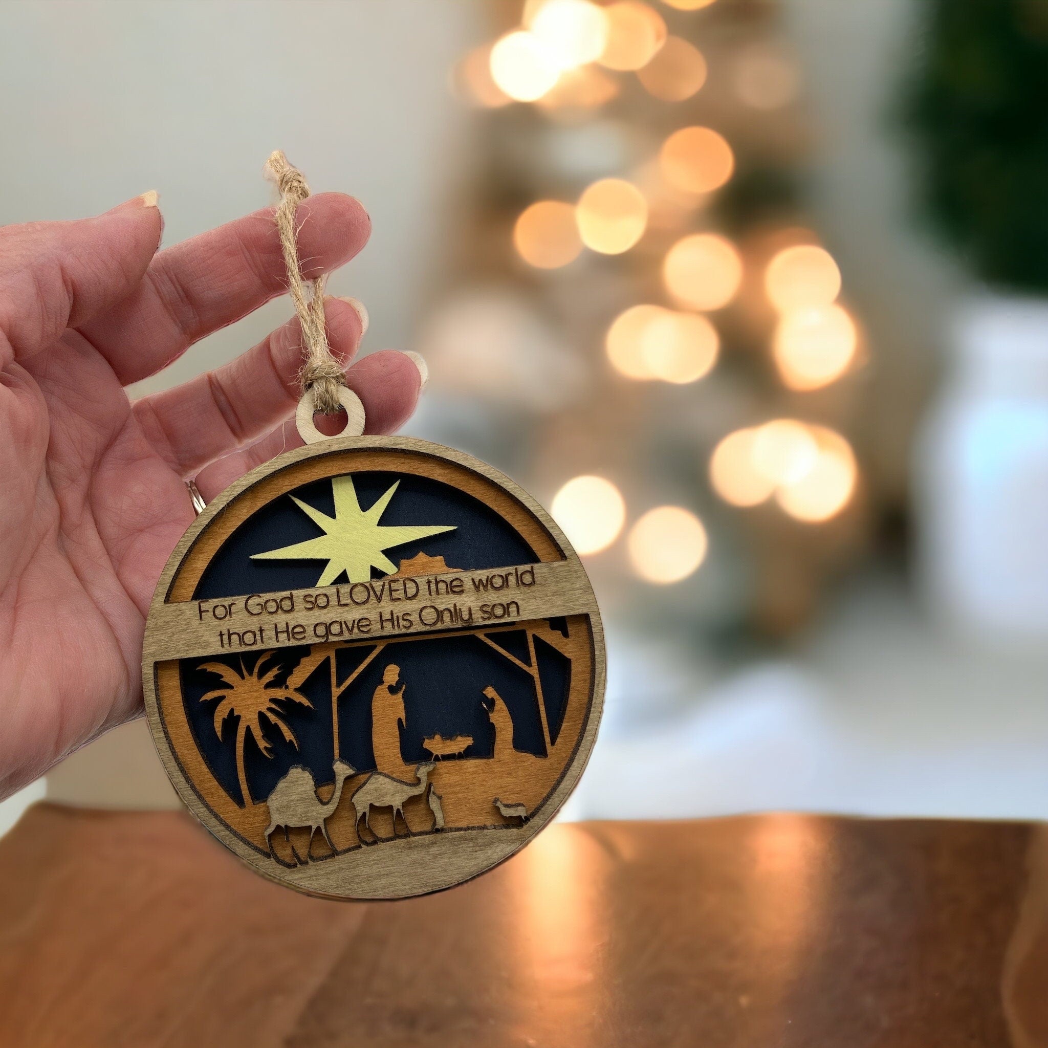 Religious Christmas tree ornament showing nativity design and engraved Bible verse.
